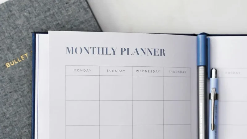 Überblick Mobile Instandhaltung 10 Sichtbar wird ein aufgeschlagener Kalender mit der Überschrift "Monthly Planner" und den Wochentagen - mit bisher keinen Einträgen - von Monday, Tuesday, Wednesday und Thursday sind sichtbar. Verschwommen sind 2 Kugelschreiber erkennbar.